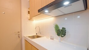 A modern kitchen with white tiles, stainless steel sink, wooden cabinets, and a black range hood. - Good Deal And Tranquil Studio Apartment Tokyo Riverside Pik 2 (Teluknaga)
