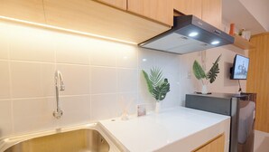 A modern kitchen with a stainless steel sink, white countertop, wooden cabinets, a black range hood, and a small potted plant. - Good Deal And Tranquil Studio Apartment Tokyo Riverside Pik 2 (Teluknaga)