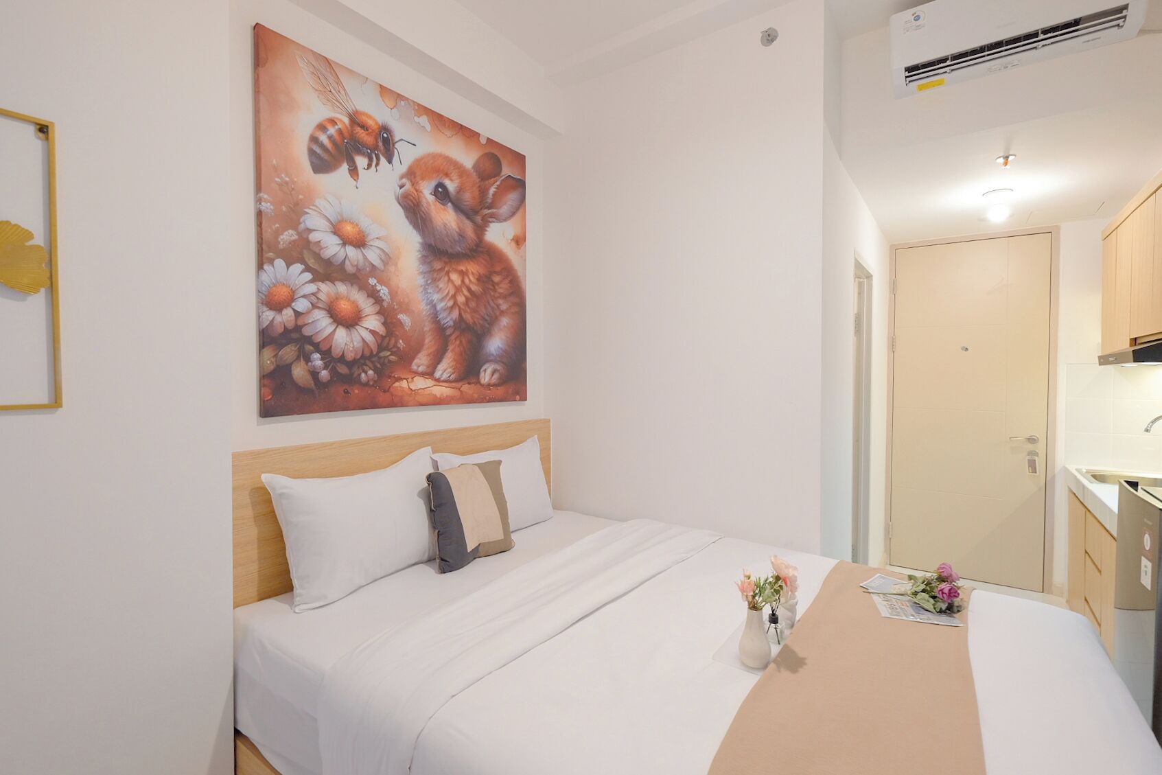 Hotelkamer met een bed, een schilderij van een bij en bloemen, een tafeltje met bloemen en een kitchenette.