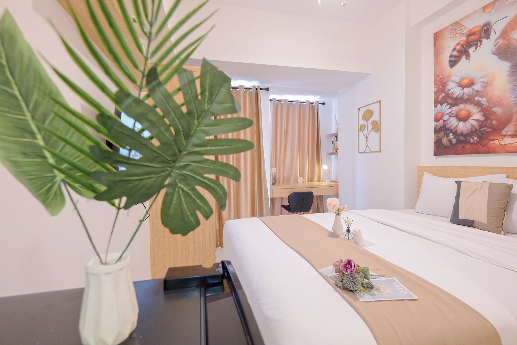 Hotellihuone, jossa on sänky, työpöytä, tuoli, suuri huonekasvi ja taulu seinällä.