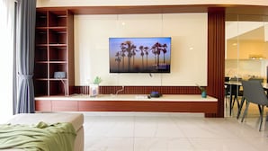 Una sala de estar moderna con un televisor de pantalla plana montado en una pared de madera, un estante empotrado con una planta y un comedor visible a través de un vano abierto.