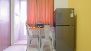 A compact kitchen with a refrigerator, two chairs, a table, and a curtain. - Comfort And Big 1Br At Green Pramuka City Apartment (Jakarta)