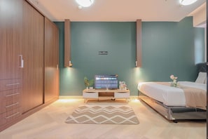 A bedroom with a bed, a desk with a computer, a wardrobe, and a green wall. - Comfort And Big 1Br At Green Pramuka City Apartment (Jakarta)