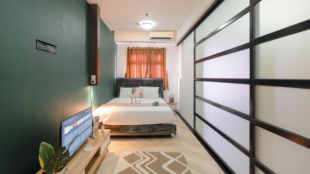 A modern bedroom with a bed, a TV, and a plant. - Comfort And Big 1Br At Green Pramuka City Apartment (Jakarta)