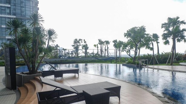 A pool area with lounge chairs and a view of palm trees and a building in the background. - Minimalist 2Br And Well Design Room At Benson Supermall Mansion Apartment (Surabaya)