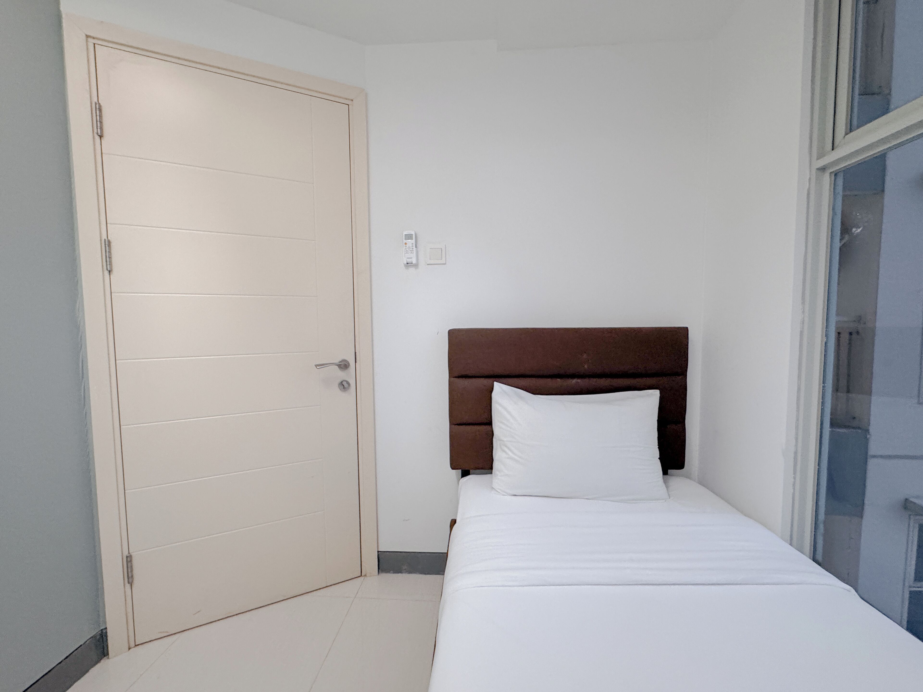 Un dormitorio pequeño y ordenado con una cama individual, cabecero de madera y puerta cerrada.