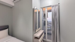 A modern hotel room with a bed, a bedside table, a mirror, and a window with curtains. - Minimalist 2Br And Well Design Room At Benson Supermall Mansion Apartment (Surabaya)