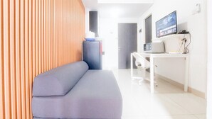 A modern room with a grey sofa, a white desk with a computer and monitor, and a wooden partition.