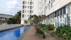 A modern building with a swimming pool, surrounded by greenery and a clear sky.