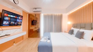 A hotel room with a large flat-screen TV mounted on the wall, a bed with a headboard, a bedside table, and a window with curtains. - Elegant 1Br Without Living Room Apartment Bintaro Embarcadero (South Tangerang)