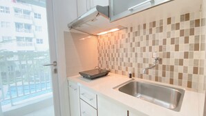 A modern kitchen with a tiled backsplash, a stainless steel sink, and white cabinetry. - Tranquil Abode 1Br Apartment At Parahyangan Residence (Bandung)