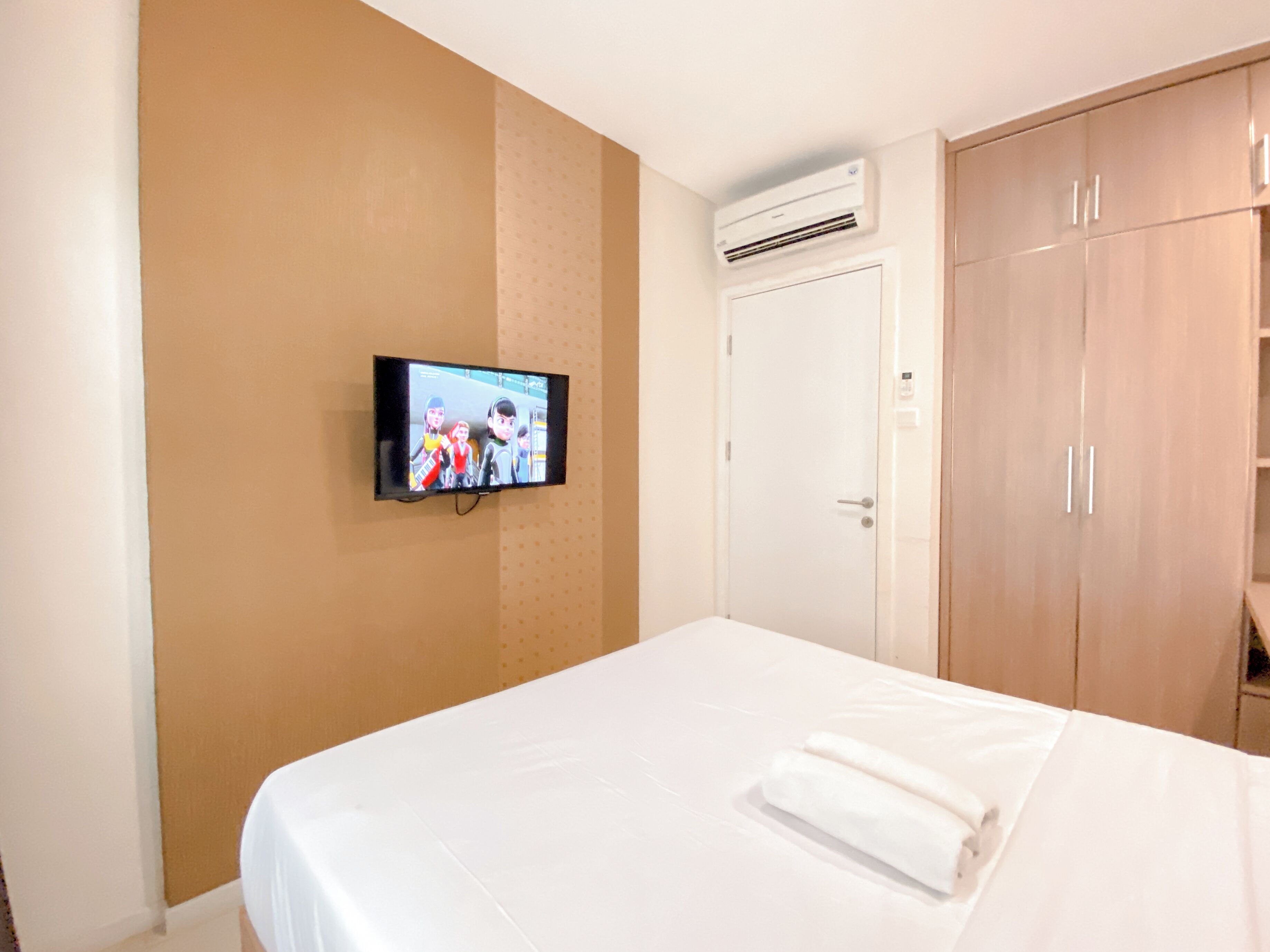 A hotel room with a bed, a television mounted on the wall, a wardrobe, and an air conditioning unit.