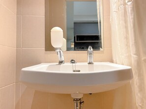 Ein Badezimmer mit einem weißen Waschbecken, einem Spiegel darüber und beige gefliesten Wänden.