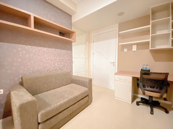 Ein Zimmer mit einem beigefarbenen Sofa, einem Schreibtisch mit Stuhl und integrierten Regalen.