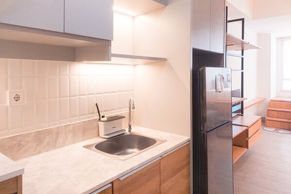 A modern kitchen with a stainless steel sink, a built-in oven, and wooden cabinets. - Comfortable Studio At Collins Boulevard Apartment (Tangerang)
