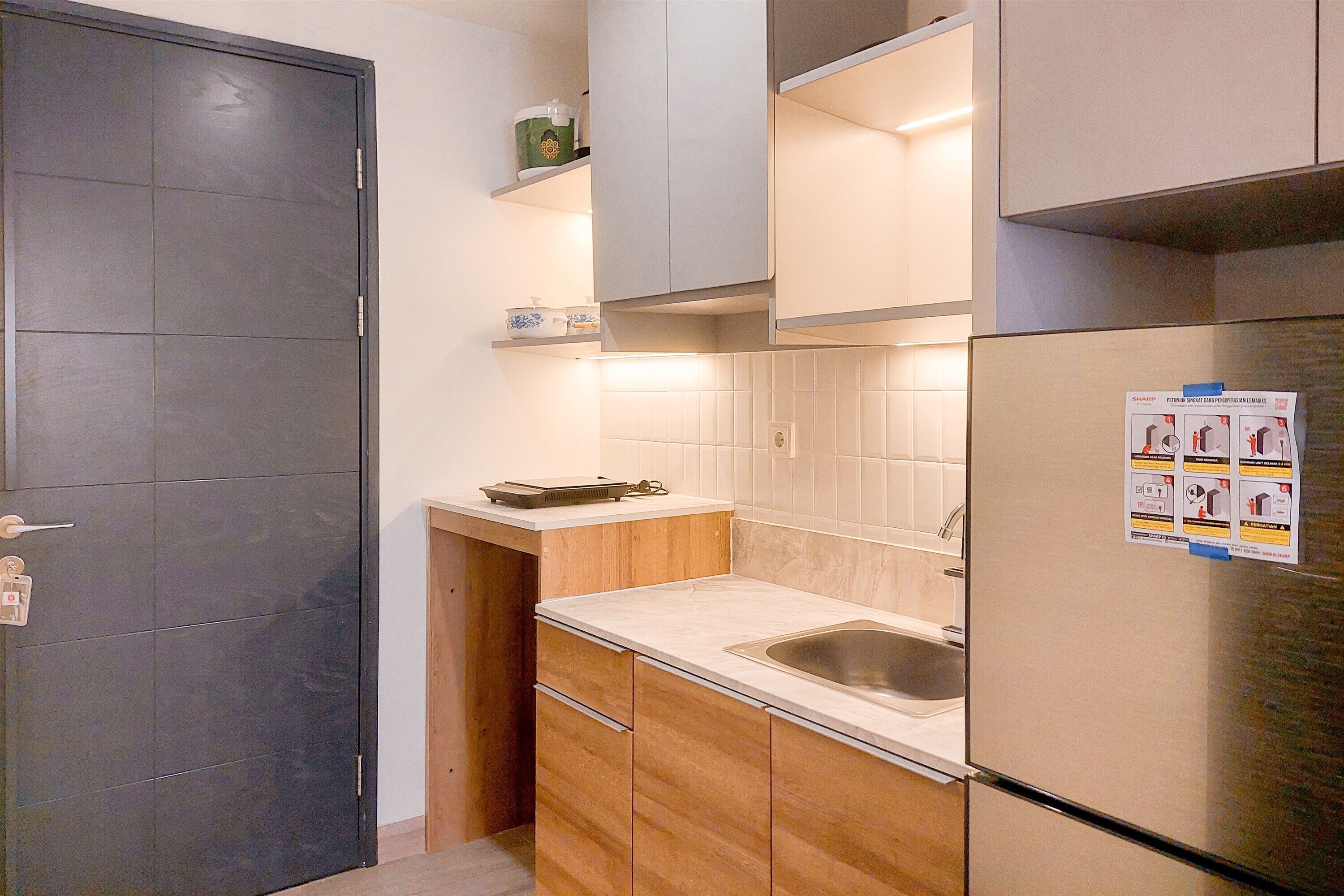 A compact kitchen with a dark door, wooden cabinets, a stainless steel refrigerator, and a sink.