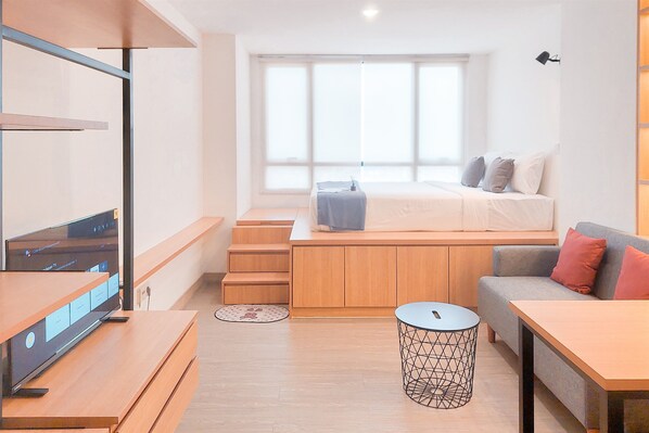 A modern, well-lit room with a bed, a sofa, a TV, and a small table.