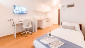 A hotel room with a bed, a desk with a chair, a television, and a kitchenette. - Best Deal Studio At Sky House Alam Sutera Apartment Near Ikea (Tangerang)