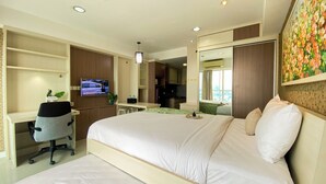 A hotel room with a large bed, a desk with a chair, a television, and a kitchenette. - Great City View Studio At Tamansari The Hive Apartment (Jakarta)