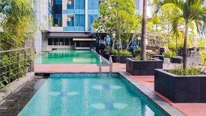 Une piscine au design moderne, entourée de verdure et bordée d’un bâtiment doté de grandes fenêtres.