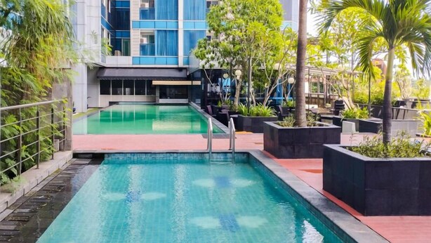 A swimming pool with a modern design, surrounded by greenery and a building with large windows. - Great City View Studio At Tamansari The Hive Apartment (Jakarta)