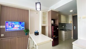 A modern kitchen with a built-in TV, a refrigerator, and a small bar area. - Great City View Studio At Tamansari The Hive Apartment (Jakarta)