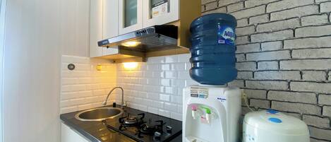 A compact kitchenette with a gas stove, a sink, a water dispenser, and a large water bottle on the counter.