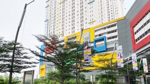 A multi-story building with a yellow and blue facade, surrounded by trees and featuring several banners.