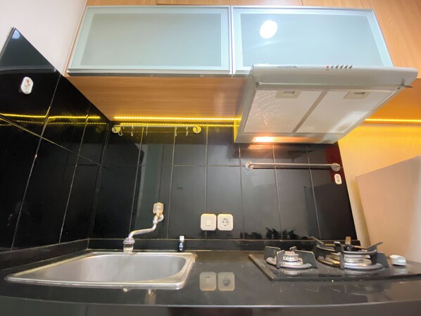 A kitchen with a black countertop, a stainless steel sink, a gas stove, and a white overhead cabinet. - Best Deal 1Br Apartment Parahyangan Residence (Bandung)