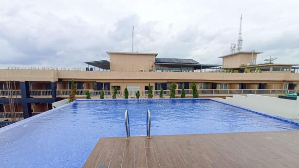 A swimming pool with two diving boards, surrounded by a building with multiple balconies and a satellite dish. - Comfortable Studio At Altuz Seturan Yogyakarta Apartment (Depok)
