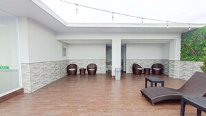 A covered outdoor seating area with wooden flooring, a glass ceiling, and a green wall with plants. - Comfortable Studio At Altuz Seturan Yogyakarta Apartment (Depok)