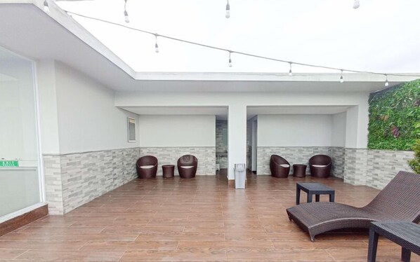 Una zona de estar al aire libre cubierta con suelo de madera, techo de cristal y una pared verde con plantas.