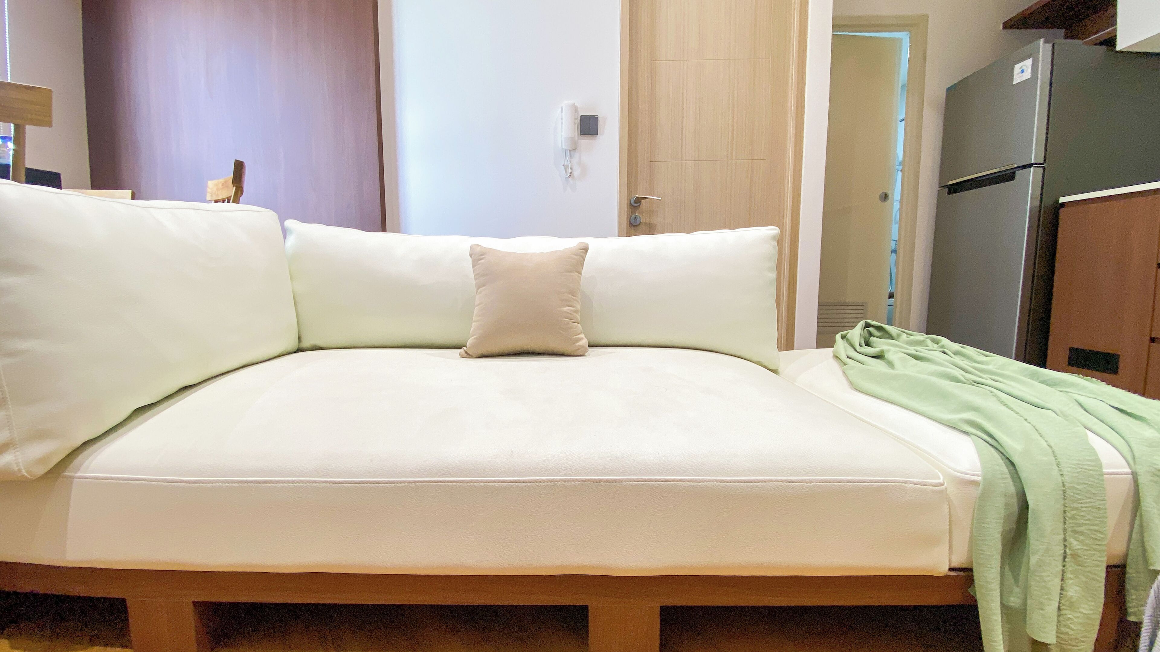 A sofa with a light-colored cushion and a single pillow, a green blanket draped over the right side, and a wooden floor.