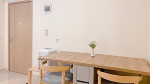 Une petite pièce, bien rangée, avec une table en bois, deux chaises, un vase blanc orné de fleurs, un lave-linge blanc et une porte en bois.