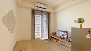 Un espace de vie compact comprenant un lit, un téléviseur à écran plat, un réfrigérateur et une plante en pot.