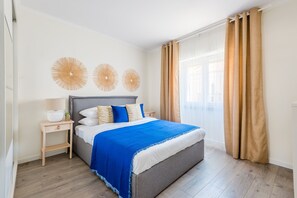 Un dormitorio con cama, mesita de noche, lámpara y ventana con cortinas.