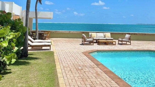A pool area with lounge chairs and a view of the ocean.