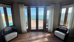 A room with a wooden floor, two white sofas, and large windows with curtains.