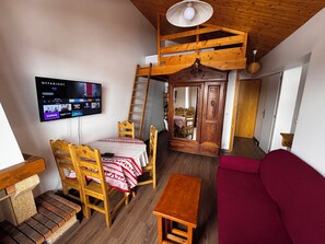 A cozy room with a wooden ceiling, a TV mounted on the wall, a wooden table, a red sofa, and a wooden ladder.