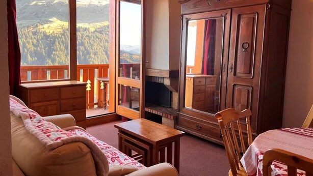 A cozy living room with a sofa, a wooden table, and a cabinet. A large window offers a view of a mountainous landscape. - Apartment Chalet Méribel Mottaret ! Ski 3 minutes' walk (Les Allues)