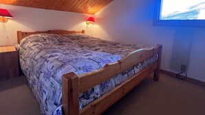 A bedroom with a wooden ceiling, a bed with a patterned bedspread, two wall-mounted lamps, and a window with a view of a snowy landscape. - Apartment Chalet Méribel Mottaret ! Ski 3 minutes' walk (Les Allues)