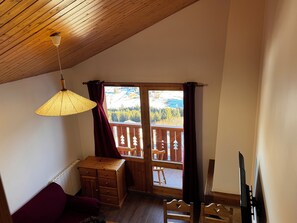Una habitación con techo y escritorio de madera, una silla, un sofá y una ventana con cortinas.
