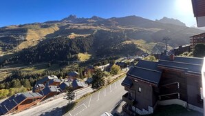 A mountain landscape with a clear sky. There are buildings with sloped roofs and a parking area in the foreground. - Apartment Chalet Méribel Mottaret ! Ski 3 minutes' walk (Les Allues)
