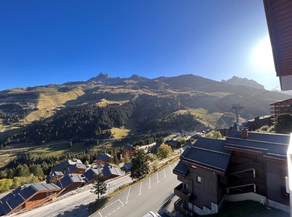 A mountain landscape with a clear sky. There are buildings with sloped roofs and a parking area in the foreground. - Apartment Chalet Méribel Mottaret ! Ski 3 minutes' walk (Les Allues)