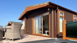 A wooden house with a hot tub, wicker furniture, and a sliding glass door. - Superior Stays at Sunset Lodge (Ilfracombe)