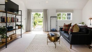 Ett modernt vardagsrum med en svart lädersoffa, ett runt soffbord, en bokhylla och utsikt över naturen genom stora fönster.