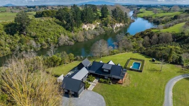 Ett modernt hus med en swimmingpool, omgivet av frodig grönska och en flod.