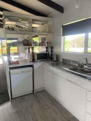 Une cuisine moderne avec des meubles blancs, un lave-vaisselle intégré, une grande fenêtre et une vue sur la verdure environnante.