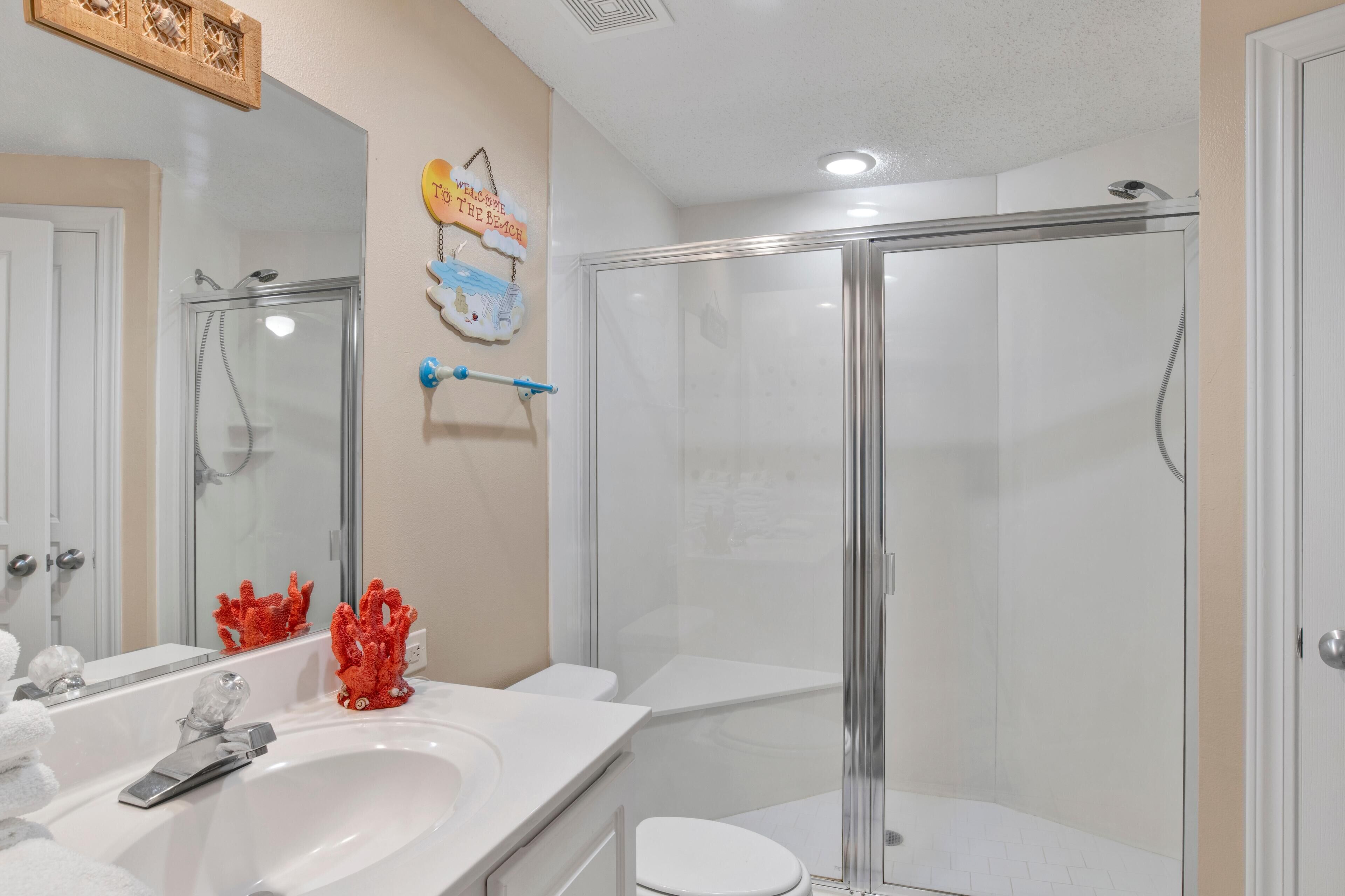 A bathroom with a glass-enclosed shower, a white sink, and a toilet.
