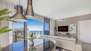 Una sala de estar moderna con una mesa de comedor de vidrio, un sofá y un amplio ventanal con vistas a la ciudad.